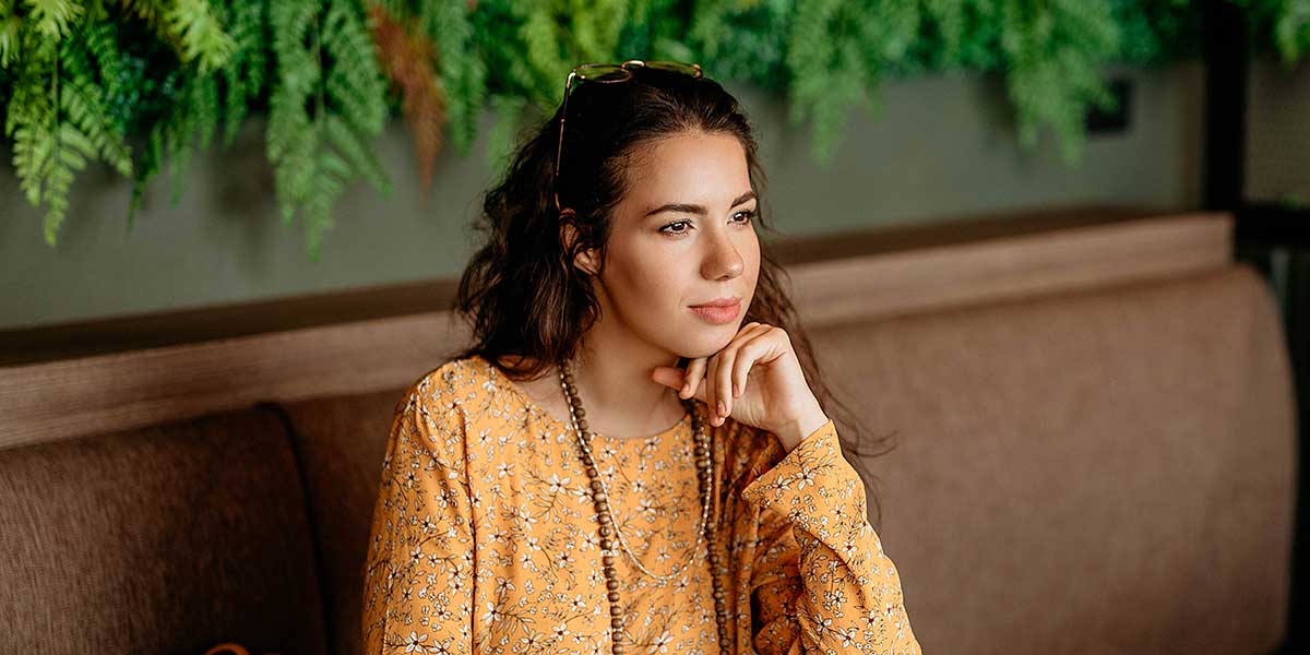 Thoughtful young woman resting her chin on her hand, reflecting on how hormone replacement therapy helps relieve brain fog.